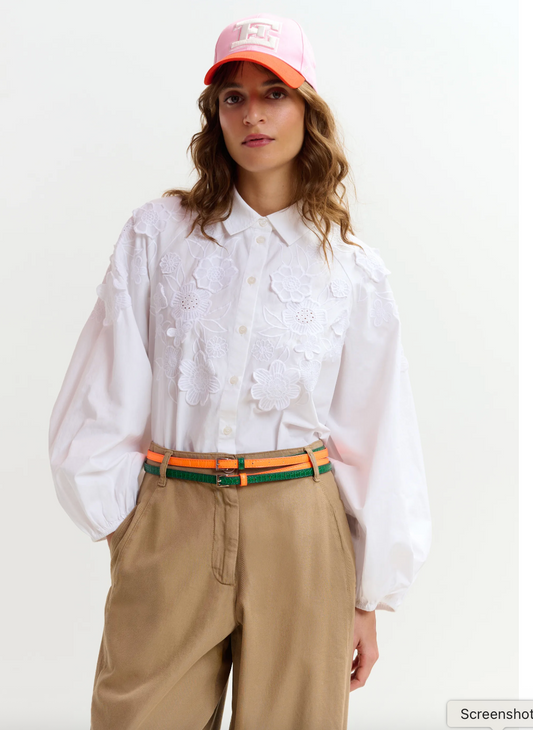 Person wearing a white shirt, beige pants, and an orange cap on a plain background from Essentiel Antwerp