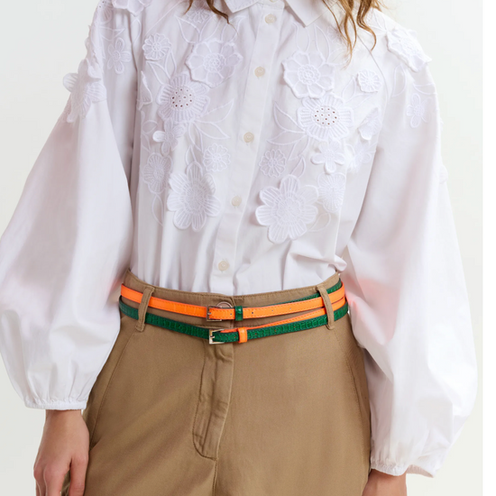 Person wearing a white blouse with floral embroidery and beige pants with an orange belt.