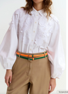 Person wearing a white blouse with floral embroidery and beige pants with an orange belt.