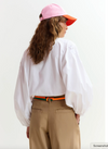Person wearing a white shirt, beige pants, and a colorful cap on a white background