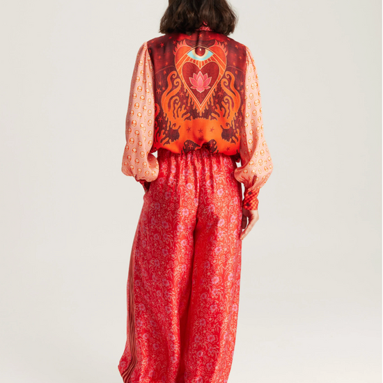 A model shown from the back wearing a red and orange patterned jumpsuit with wide-leg pants and black pointed-toe heels, against a plain light gray studio background.