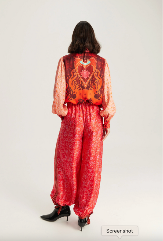 A model shown from the back wearing a red and orange patterned jumpsuit with wide-leg pants and black pointed-toe heels, against a plain light gray studio background.