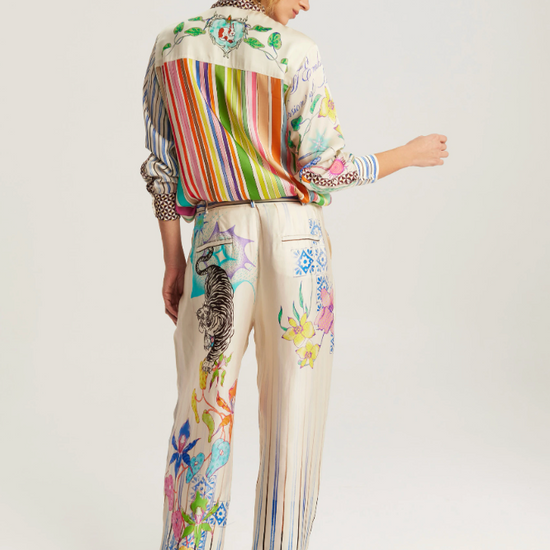 A model shown from the back wearing a matching cream-colored two-piece set featuring colorful striped and floral prints, paired with brown leather boots, against a light gray studio background.