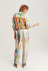 A model shown from the back wearing a matching cream-colored two-piece set featuring colorful striped and floral prints, paired with brown leather boots, against a light gray studio background.