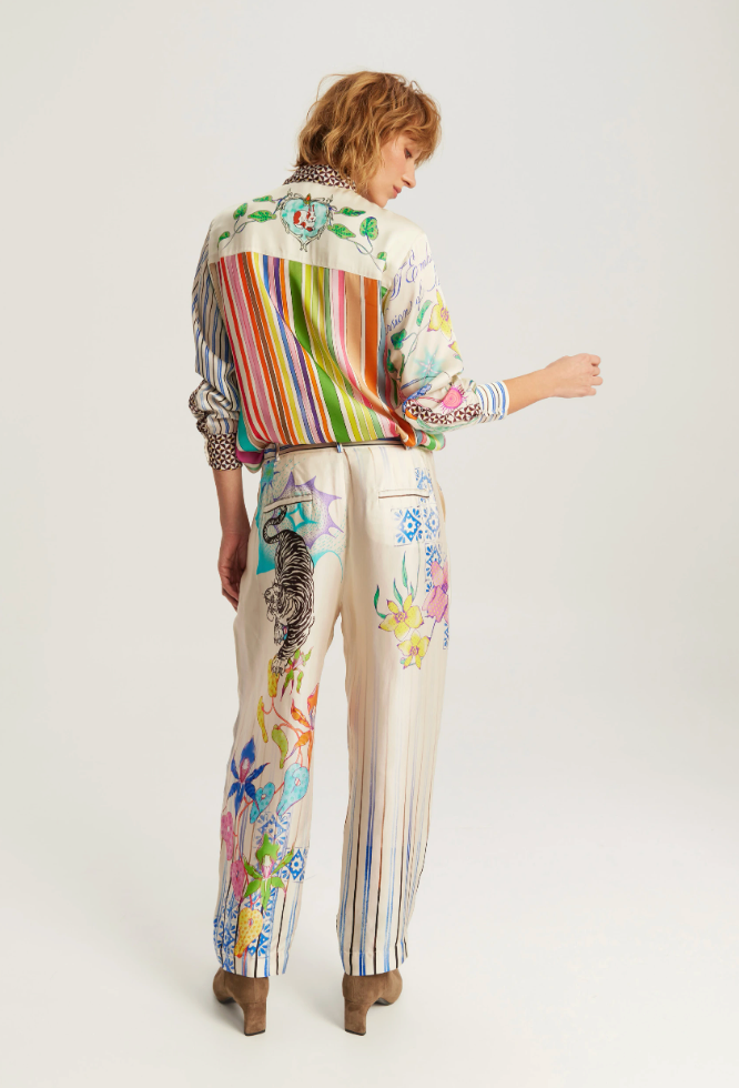 A model shown from the back wearing a matching cream-colored two-piece set featuring colorful striped and floral prints, paired with brown leather boots, against a light gray studio background.
