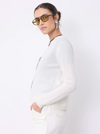 A model wearing a white knit long-sleeve cardigan and matching white trousers, styled with yellow-tinted sunglasses and silver hoop earrings against a plain white background.