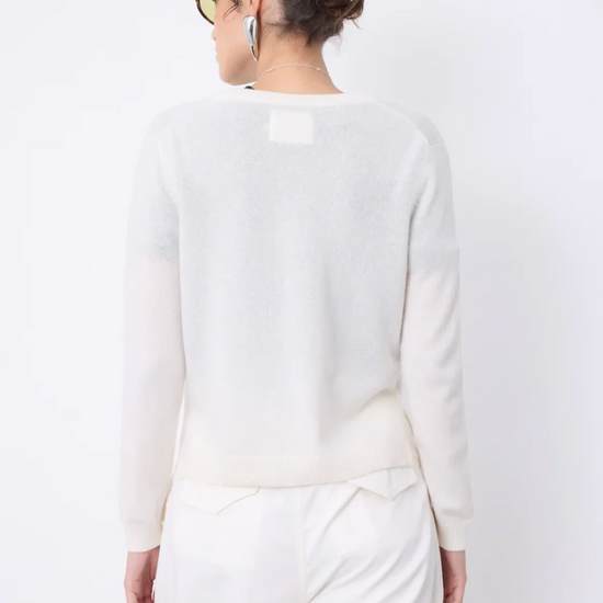 A woman shown from the back wearing a light cream knit sweater and matching cream trousers against a plain white studio background.