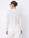 A woman shown from the back wearing a light cream knit sweater and matching cream trousers against a plain white studio background.