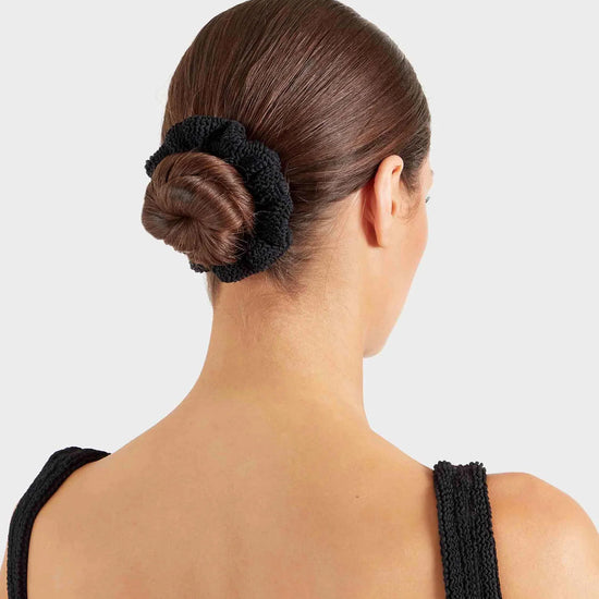 Woman with a bun held in place by a black hair tie against a light gray background