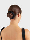 Woman with a bun held in place by a black hair tie against a light gray background