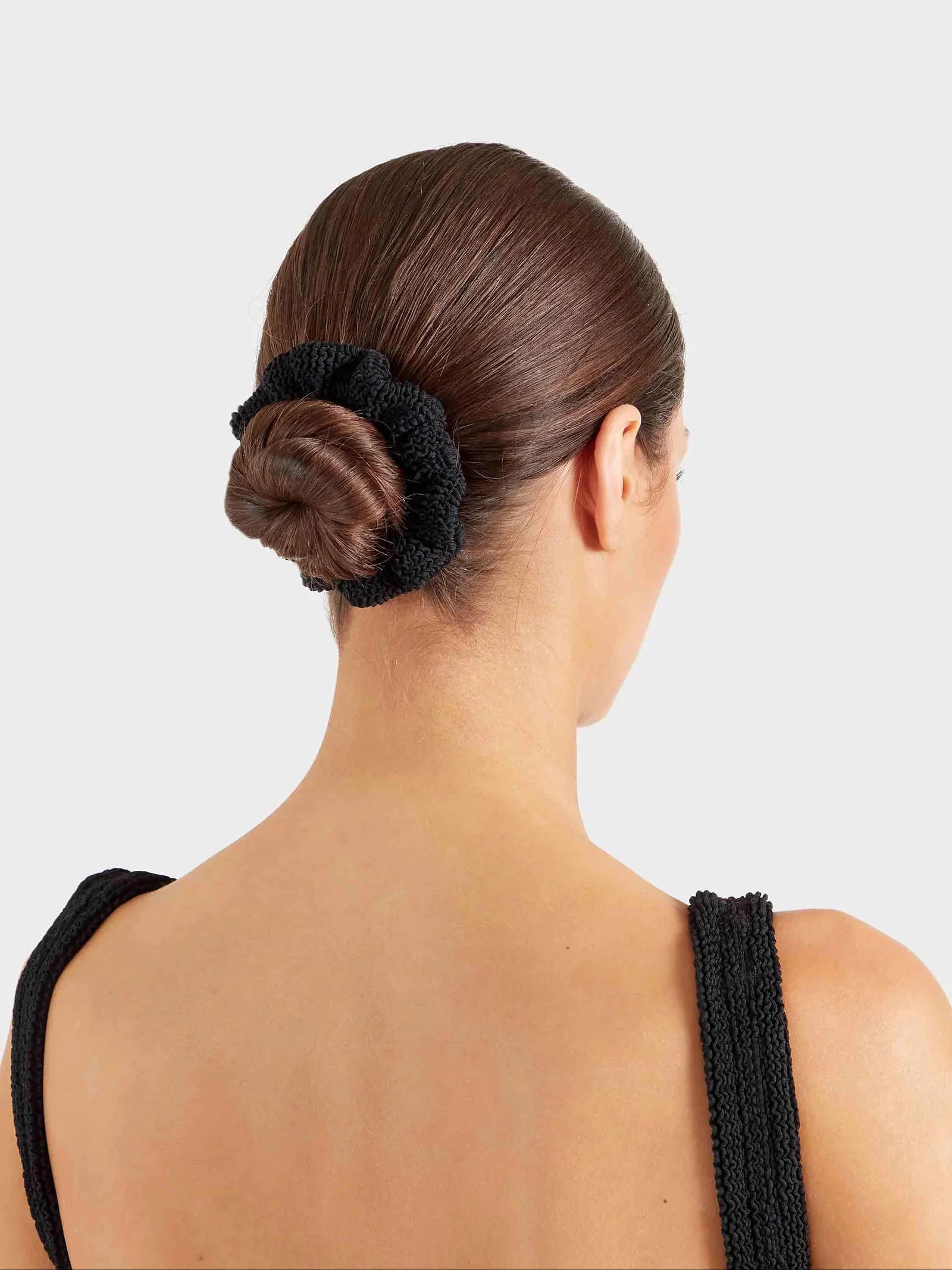 Woman with a bun held in place by a black hair tie against a light gray background