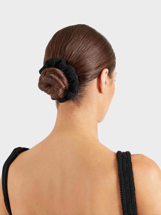 Woman with a bun held in place by a black hair tie against a light gray background