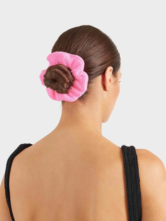 Woman with a pink hair towel wrapped around her bun against a light gray background