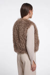 A woman shown from the back wearing a shaggy, cropped taupe-brown vest over a light beige long-sleeve top and beige trousers, against a plain white studio background.