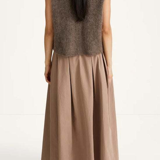 A woman shown from the back wearing a sleeveless taupe-brown fuzzy knit vest over a long taupe pleated skirt, paired with dark brown shoes, against a plain white studio background.