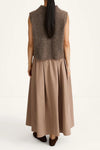 A woman shown from the back wearing a sleeveless taupe-brown fuzzy knit vest over a long taupe pleated skirt, paired with dark brown shoes, against a plain white studio background.