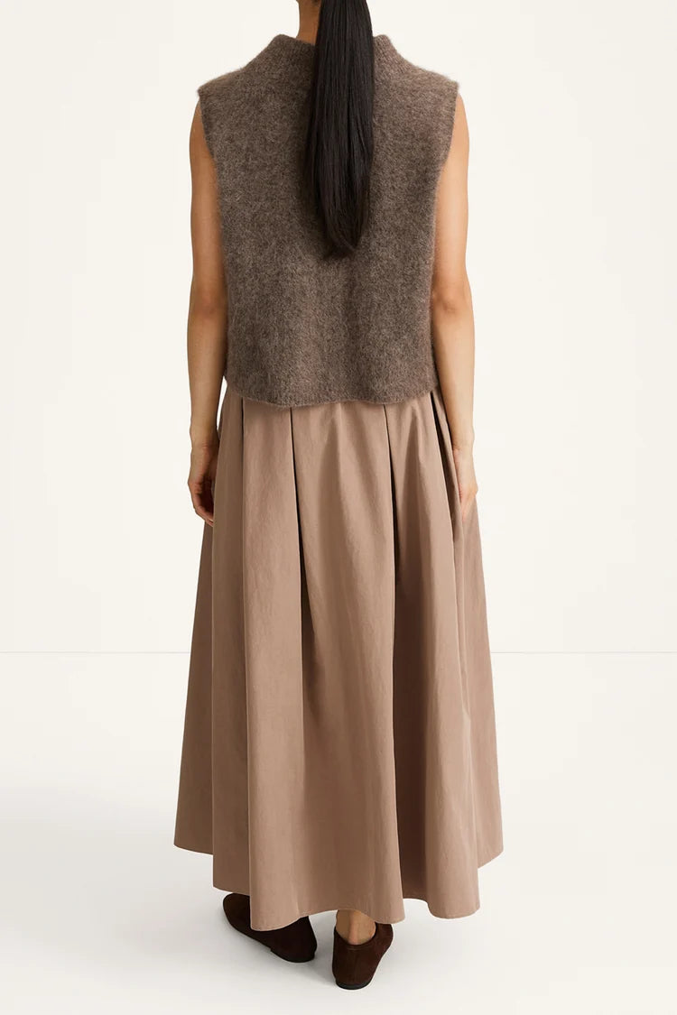 A woman shown from the back wearing a sleeveless taupe-brown fuzzy knit vest over a long taupe pleated skirt, paired with dark brown shoes, against a plain white studio background.