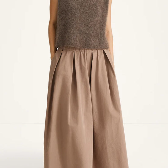 Woman wearing a brown sleeveless top and long skirt on a white background