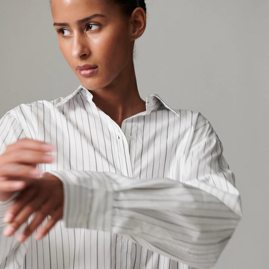 Woman wearing a white and gray striped shirt against a gray background