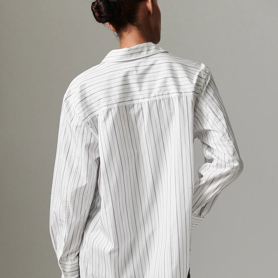 Person wearing a white shirt with black vertical stripes against a gray background