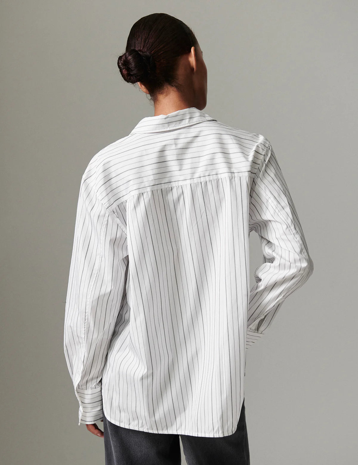 Person wearing a white shirt with black vertical stripes against a gray background