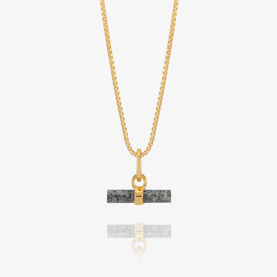 A gold chain necklace with a rectangular dark gray stone pendant featuring a gold split ring and clasp, displayed against a light gray background with a soft reflection below.