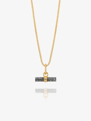 A gold chain necklace with a rectangular dark gray stone pendant featuring a gold split ring and clasp, displayed against a light gray background with a soft reflection below.