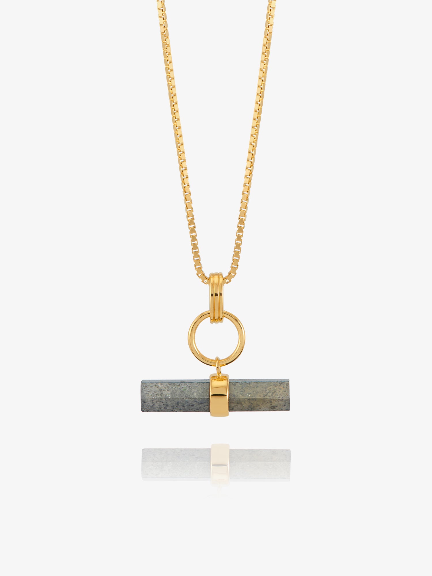 A gold chain necklace with a horizontal bar pendant featuring a dark gray stone inlay and a gold accent, shown against a light gray background with a soft reflection below.