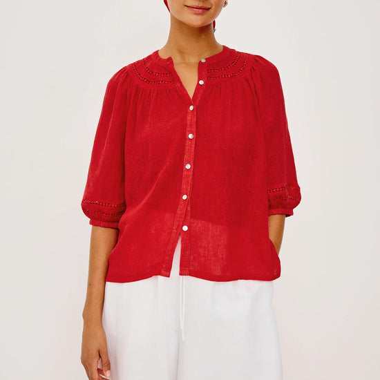 Woman wearing a red blouse and white shorts with a blue and white checkered headscarf on a light background