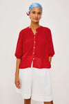 Woman wearing a red blouse and white shorts with a blue and white checkered headscarf on a light background