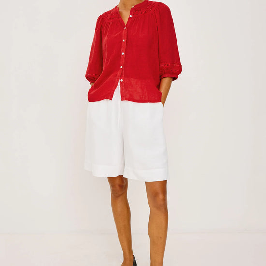 Woman wearing a red shirt, white shorts, and black shoes on a plain background