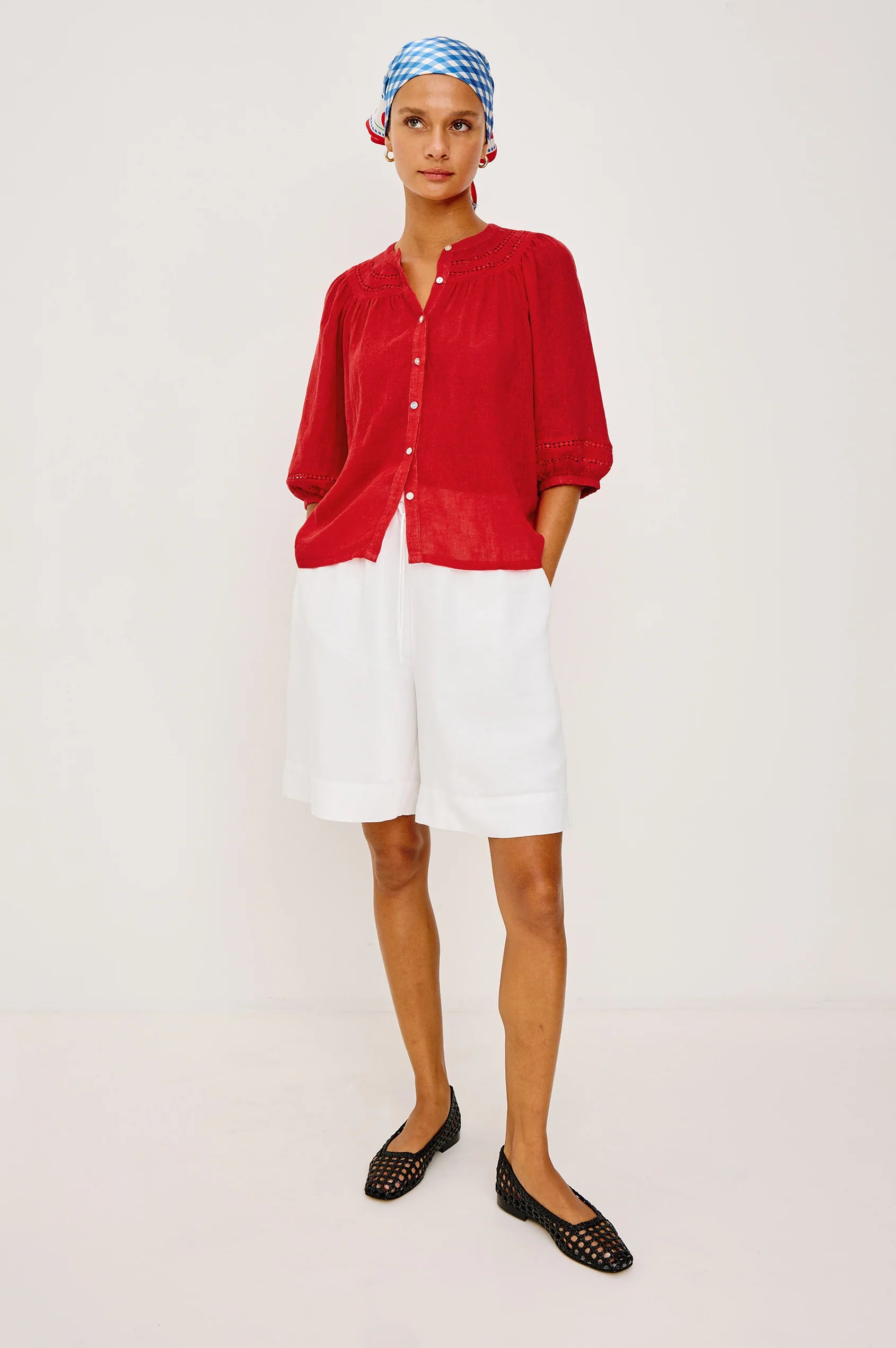 Woman wearing a red shirt, white shorts, and black shoes on a plain background