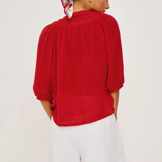 Person wearing a red top and white shorts with a patterned headscarf on a plain background