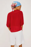 Person wearing a red top and white shorts with a patterned headscarf on a plain background