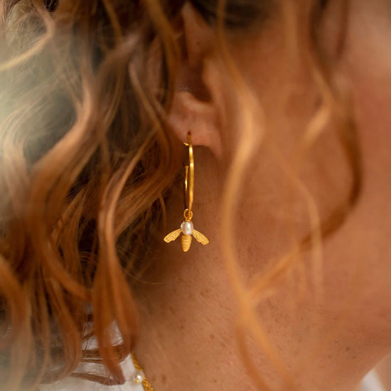 Large gold hoop earrings with flying bee pendants and a rice pearl drop with butterfly earring fastenings