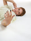 A woman lying on a white studio floor wearing a fluffy cream top and displaying gold jewelry, including a thick gold ring and a gold bangle.