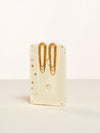 A cream-colored cassette tape-shaped desk organizer holding two gold paperclips, set against a clean off-white background.