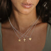 Close-up of a woman wearing three necklaces with star, cross, and heart pendants from Anna Beck