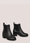 A pair of black leather Chelsea ankle boots with elastic side panels and low block heels, displayed against a solid pale pink background.