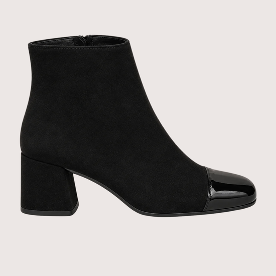 A pair of black ankle boots with a block heel and glossy patent leather toe caps, shown against a solid light beige background.