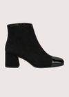 A pair of black ankle boots with a block heel and glossy patent leather toe caps, shown against a solid light beige background.