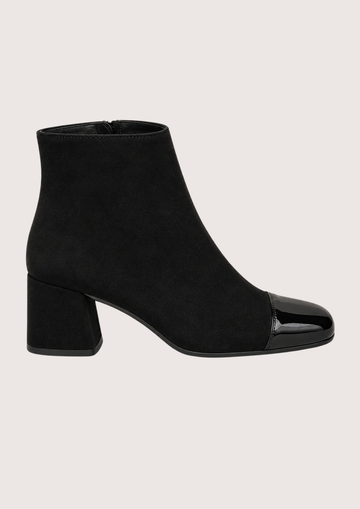 A pair of black ankle boots with a block heel and glossy patent leather toe caps, shown against a solid light beige background.