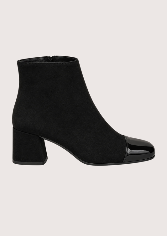 A pair of black ankle boots with a block heel and glossy patent leather toe caps, shown against a solid light beige background.