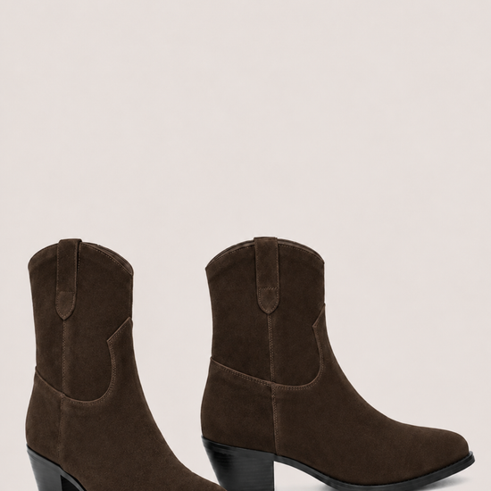 A pair of dark brown suede western-style ankle boots with low block heels, shown from the side and back-three-quarter angles against a solid light beige background.