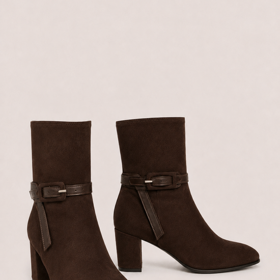 A pair of dark brown suede ankle boots with block heels and a matching faux-leather buckle strap around the ankle, shown against a plain light beige background.