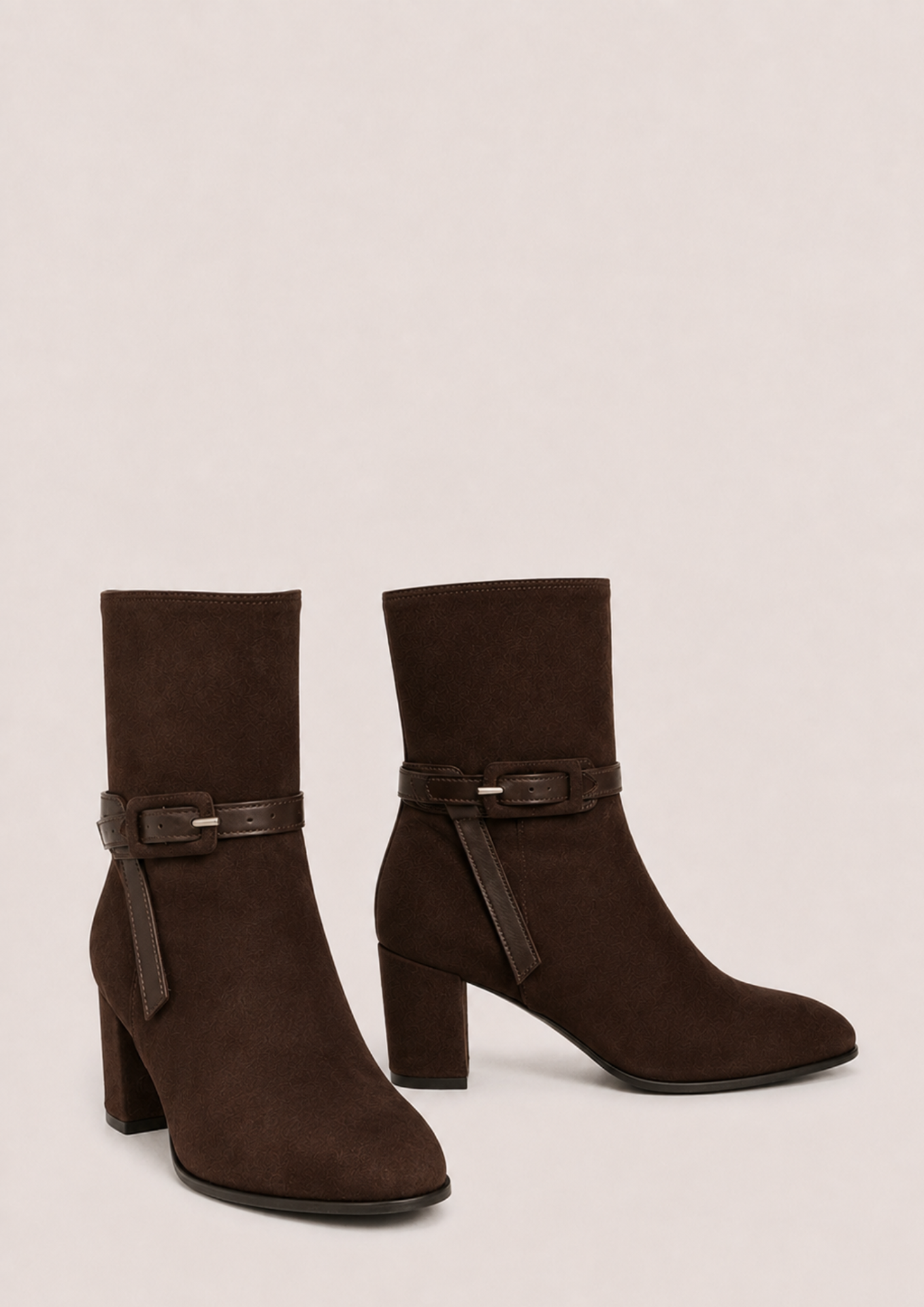 A pair of dark brown suede ankle boots with block heels and a matching faux-leather buckle strap around the ankle, shown against a plain light beige background.
