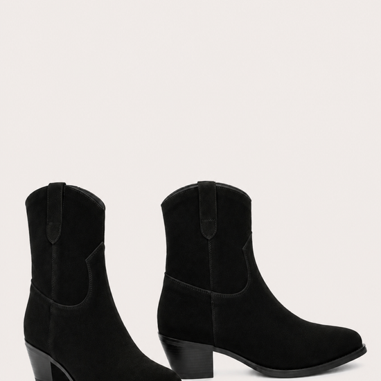 A pair of black suede western-style ankle boots with low block heels, shown against a solid off-white background.