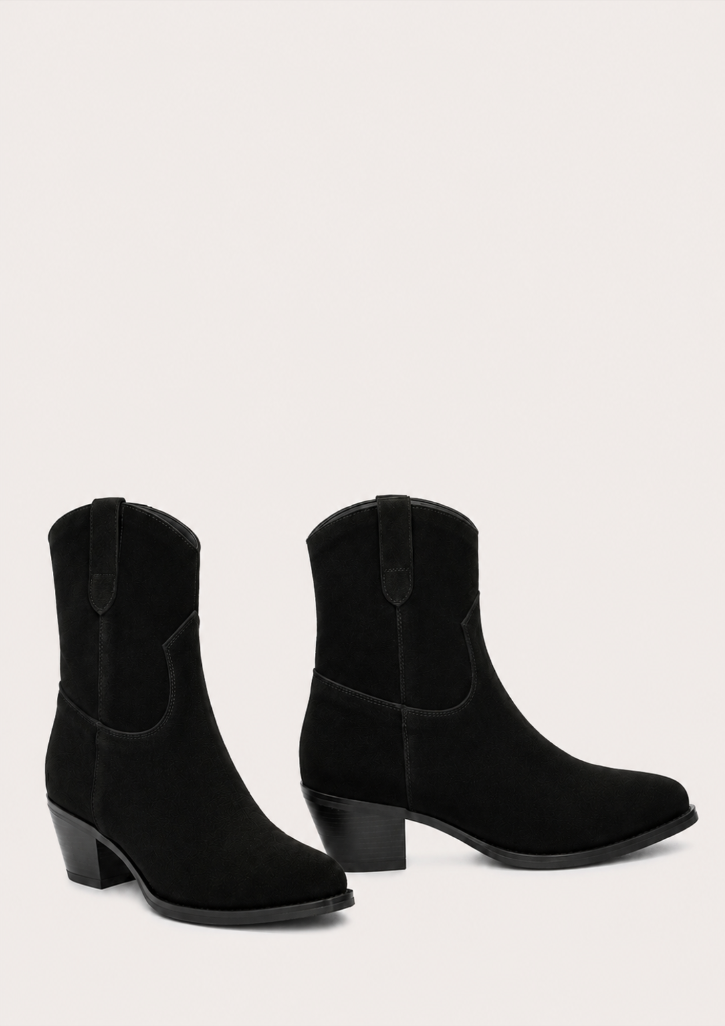 A pair of black suede western-style ankle boots with low block heels, shown against a solid off-white background.