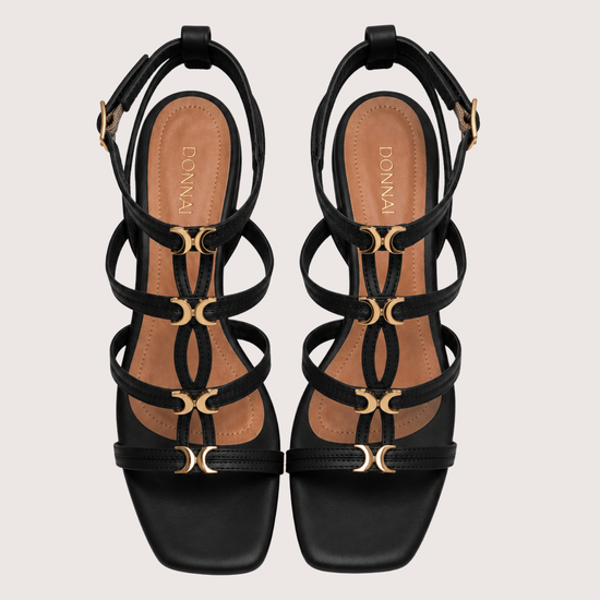Black strappy sandals with gold accents on a light gray background