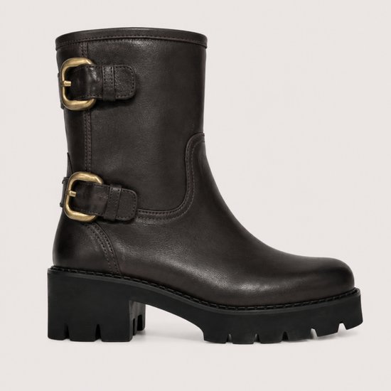 A black leather ankle boot with a chunky lug sole and two gold-tone buckle straps on the side, shown against a light gray background.